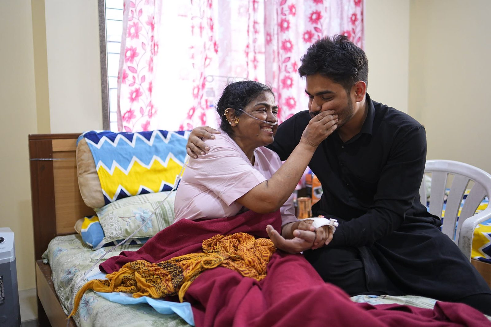 A patient smiling in a hospital bed, holding hands with a family member seated beside her