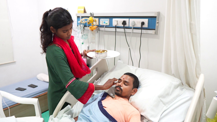 A caregiver bringing a meal and tending to a patient resting in a hospital bed